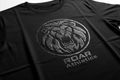 Black tee with large HD ink chest logo, 3D relief visible in raking studio light